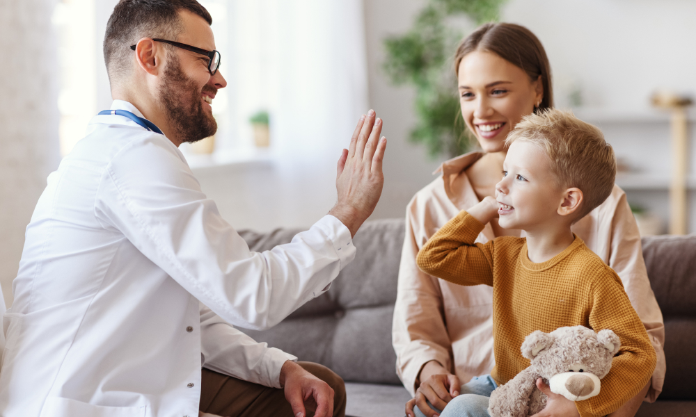Physician high-fiving a boy with mother behind him