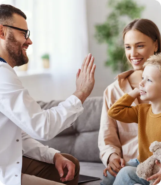 Doctor giving small boy a high-five with mother behind the boy