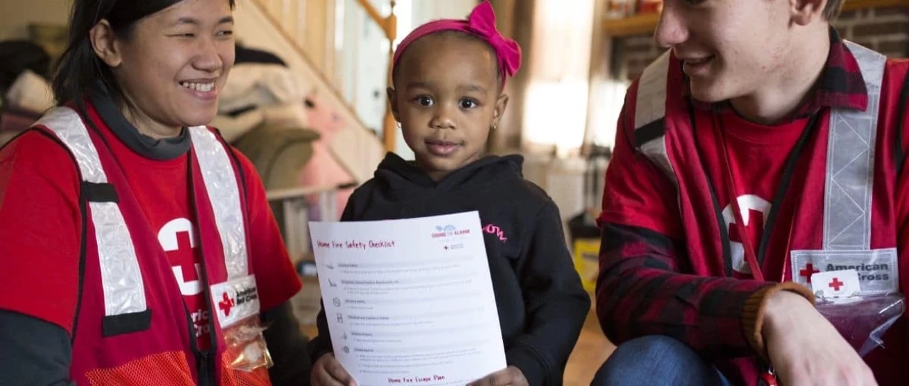 child between two red cross volunteers holding a safety checklist